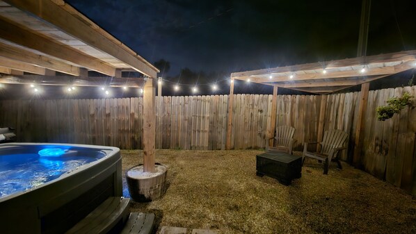 A backyard with a hot tub, wooden deck, and string lights.