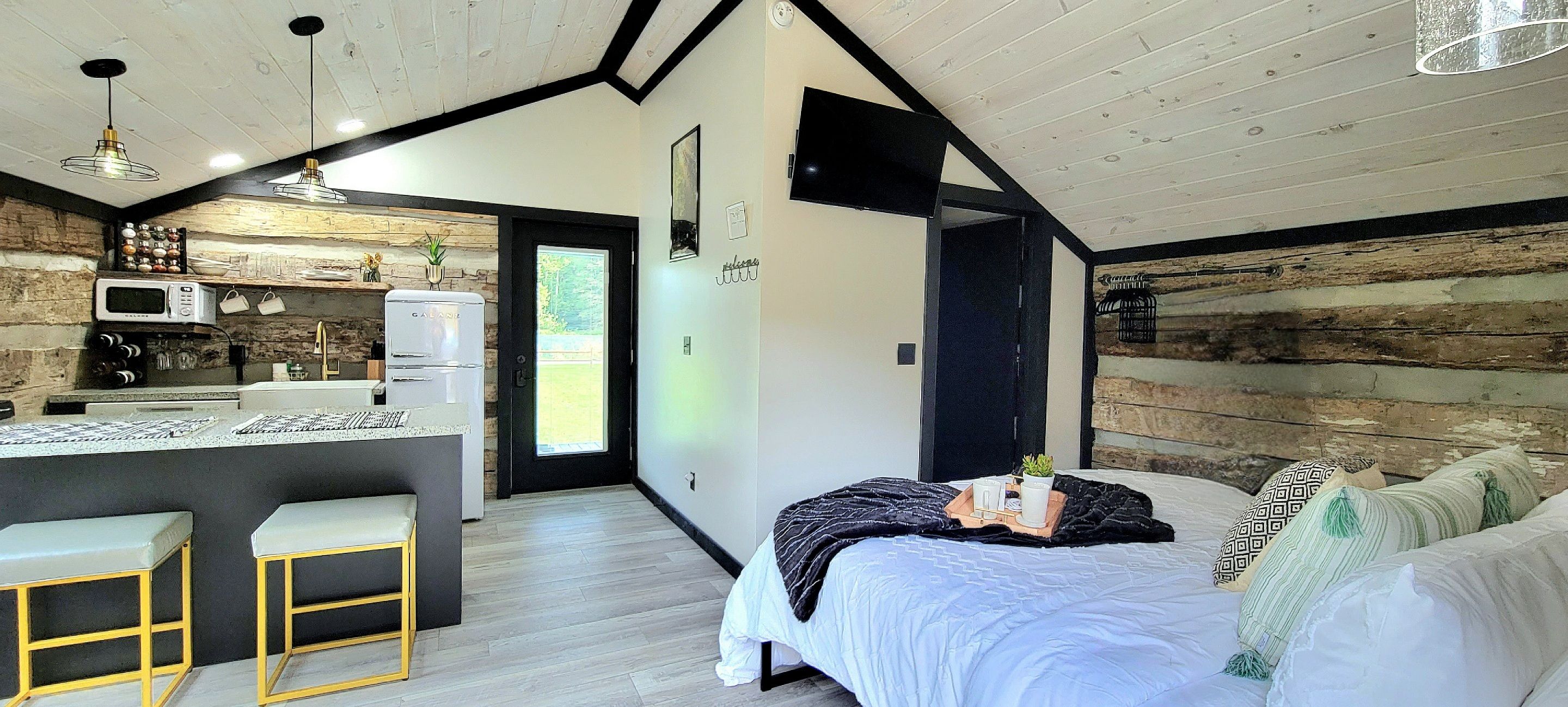A modern bedroom with a bed, bedside table, and a view of a kitchen area.
