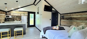 A modern bedroom with a bed, bedside table, and a view of a kitchen area.