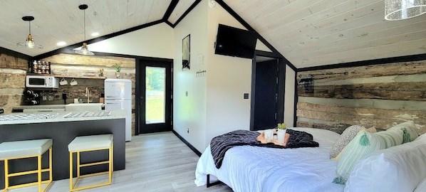 A modern bedroom with a bed, bedside table, and a view of a kitchen area.