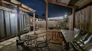 An outdoor patio area with a grill, seating, and a wooden fence.