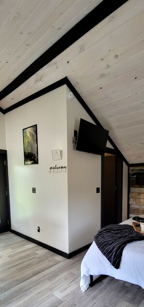 A modern bedroom with a sloped ceiling, a bed with a striped blanket, a mounted TV, and a welcome sign on the wall.