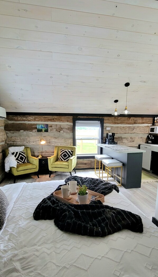 A cozy room with a bed, two chairs, a coffee table, and a kitchen area with a window.