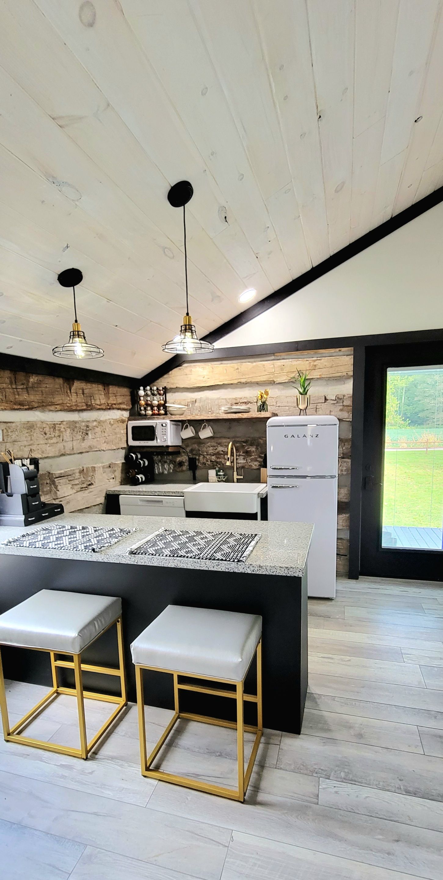 Une cuisine moderne dotée d’un îlot central, de luminaires suspendus et offrant une vue sur l’extérieur.