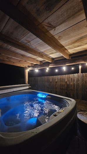 A hot tub with a wooden ceiling and a wooden fence in the background.