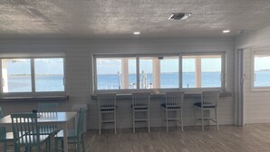 Een kamer met uitzicht op zee, houten vloer, witte muren en een eethoek met stoelen en een tafel.