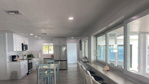 Een moderne keuken met witte kasten, een eethoek met lichtblauwe stoelen, en een groot raam met uitzicht op een waterlichaam.