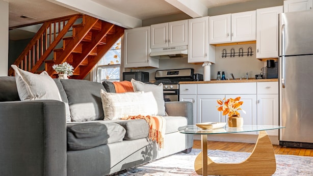 A modern living room with a gray sofa, a glass coffee table, and a patterned rug. A wooden staircase leads to an upper level. - Walk to Brady St, 2-story upper flat, Sleeps 7! (Milwaukee)