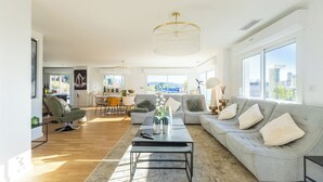 Un salon spacieux avec un canapé gris, une table basse et un coin repas à l’arrière-plan.
