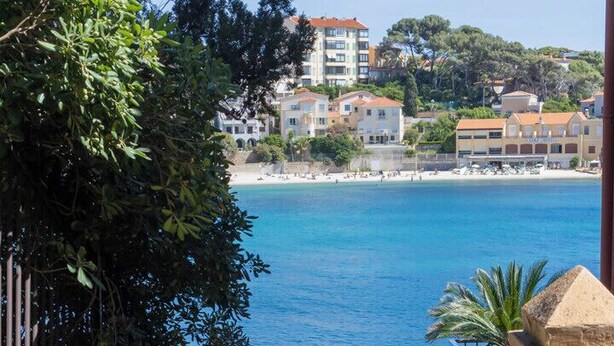 Une vue sur la côte, avec une mer bleue et limpide, un escalier descendant vers la plage et des bâtiments en arrière-plan.