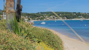 Un paysage côtier avec une plage de sable, des palmiers et une mer bleue et limpide où naviguent des bateaux.