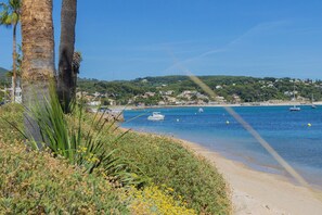 Eine Küstenlandschaft mit Sandstrand, Palmen und einem klaren, blauen Meer mit Booten.