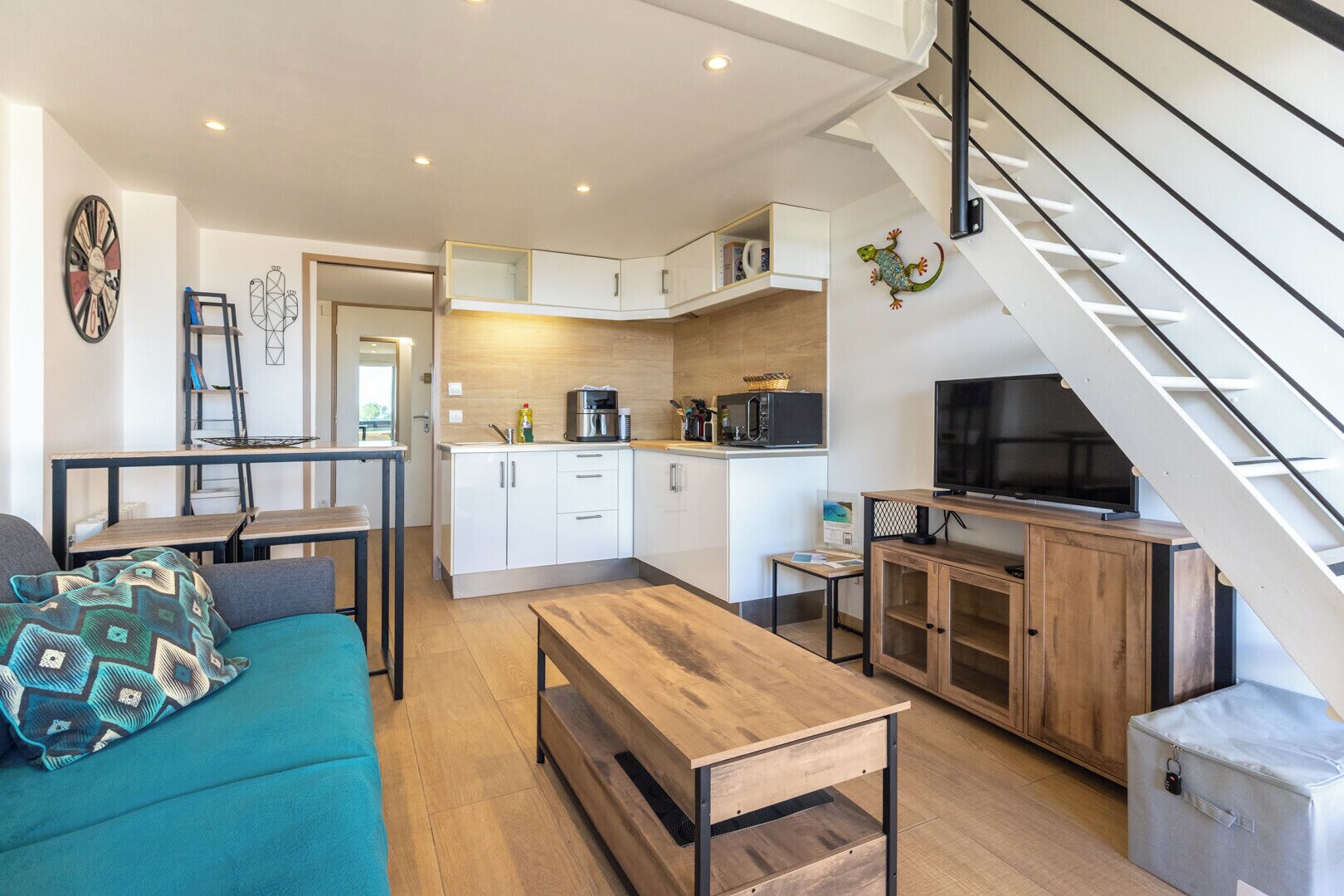 Un espacio habitable compacto con kitchenette, comedor, sofá y escalera.