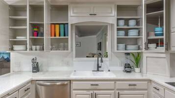A modern kitchen with white cabinetry, a central island with a sink, and open shelving with dishes and kitchenware.