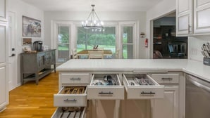 Una cocina con armarios blancos, una isla central con cajones y vista a un comedor.