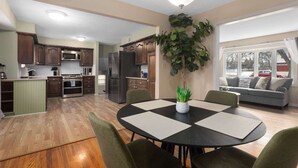 A modern kitchen with wooden cabinets, stainless steel appliances, and a dining area with a round table and chairs. - Spacious Home_2 Living Rooms_Sleeps 14_7 KingBeds (Overland Park)