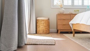 Een slaapkamer met een houten bed, een rieten bijzettafeltje en een raam met jaloezieën.