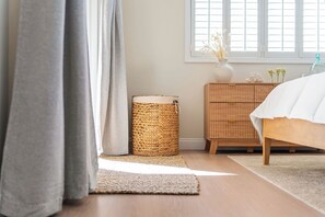 Ein Schlafzimmer mit einem hölzernen Bett, einem Korbtisch und einem Fenster mit Jalousien.