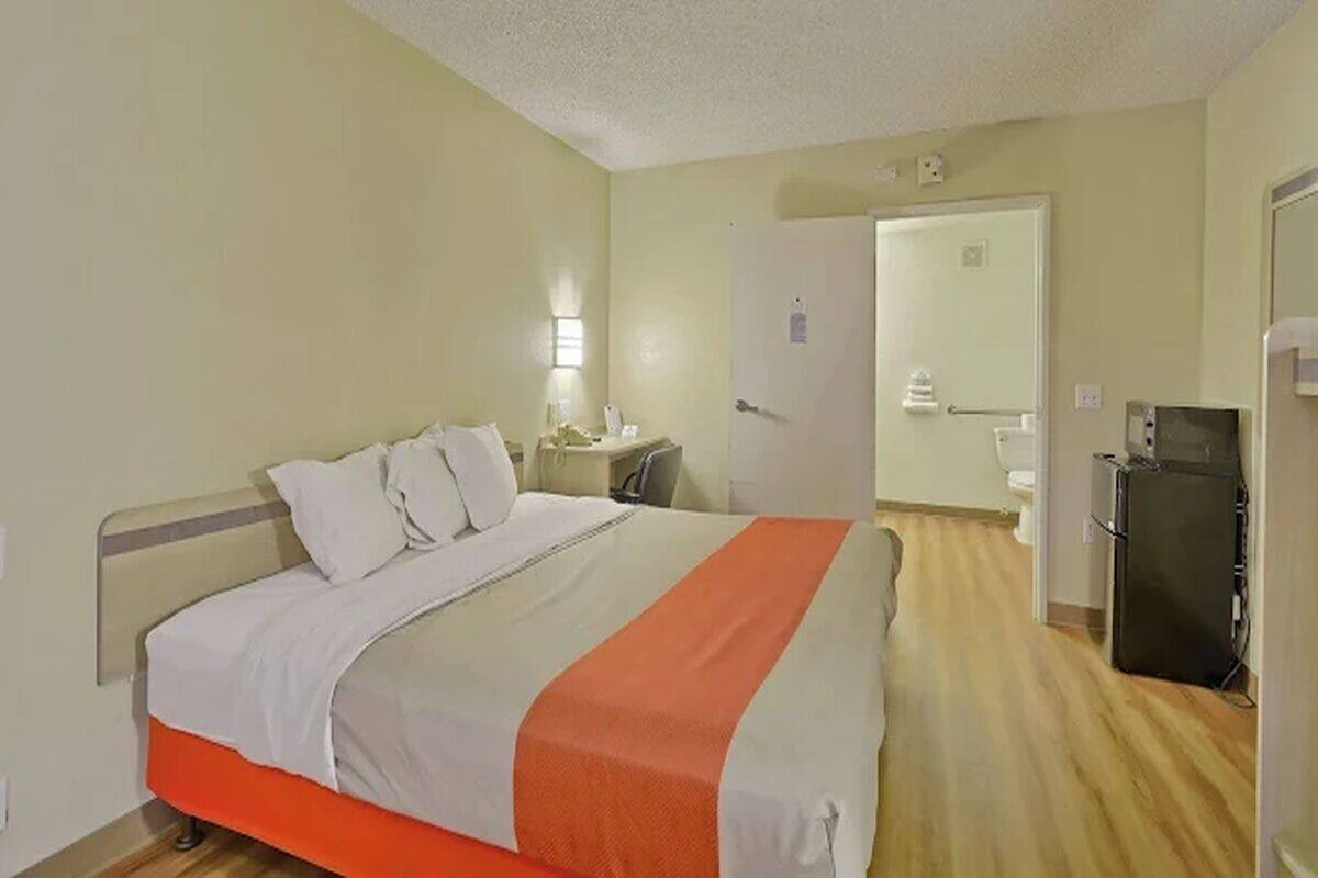 Habitación de hotel con cama, escritorio, silla, refrigerador y puerta que da a un baño.