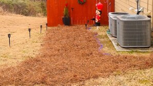 A backyard with a red fence, a small Christmas tree, and two air conditioning units.