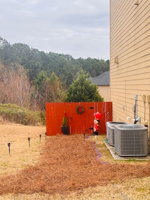 A backyard with a red fence, a small Christmas tree, and two air conditioning units.