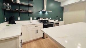 A modern kitchen with white cabinets, a stainless steel range hood, and a large island.