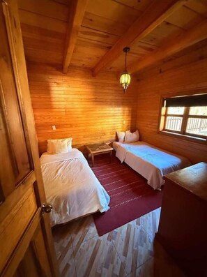 A wooden cabin room with two beds, a small table, and a window.