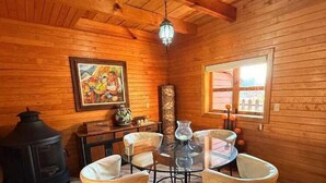 Un intérieur chaleureux, avec des murs en bois, une table ronde en verre entourée de quatre chaises, une cheminée et un tableau accroché au mur.
