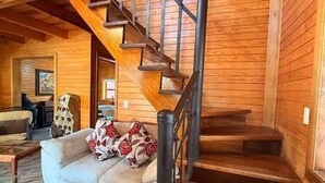 Un intérieur en bois avec un escalier, un canapé agrémenté de coussins à motifs floraux et une table à manger.