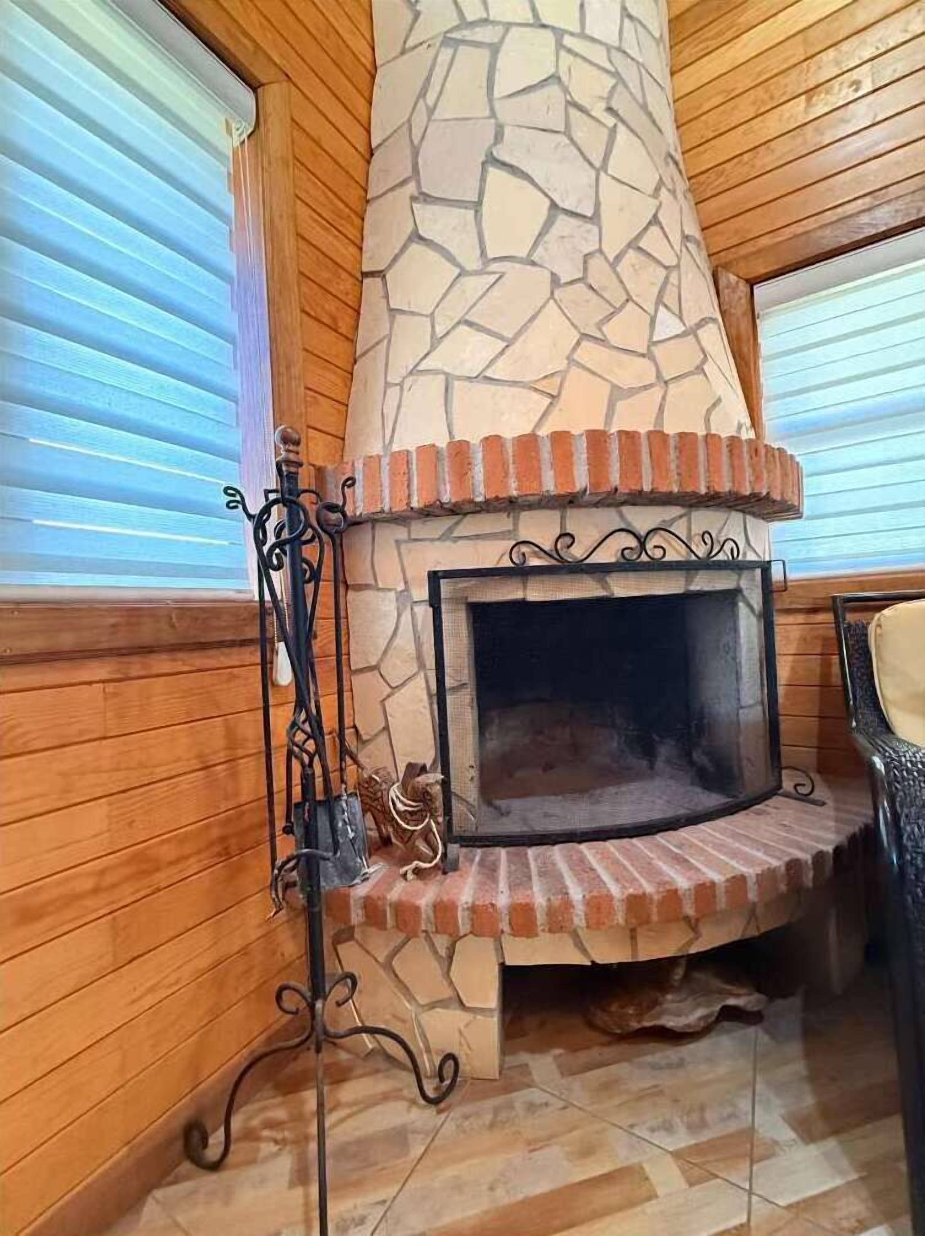 Een stenen openhaard met een fundering van baksteen, aan weerszijden omlijst door houten wanden en een metalen standaard waarop een decoratief object staat.