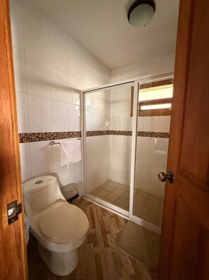 A bathroom with a toilet, a shower with a glass door, and a tiled floor.