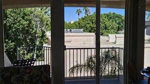Habitación con puerta de vidrio corrediza que da a un balcón con vista a palmeras y un edificio.