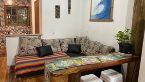 A cozy living area with a sofa, a colorful woven table runner, and a framed wave painting on the wall. - Cabin surrounded by nature, close to the beach and dunes. (Imbituba)