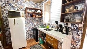A compact kitchen with a microwave, stove, sink, and shelves with dishes. - Cabin surrounded by nature, close to the beach and dunes. (Imbituba)