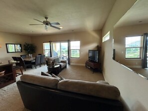 A spacious living room with a large sofa, a dining table with chairs, a television, and large windows offering a view of the outdoors. - B07-Spacious 3-bedroom townhome in tranquil Quincy with AC (Quincy)
