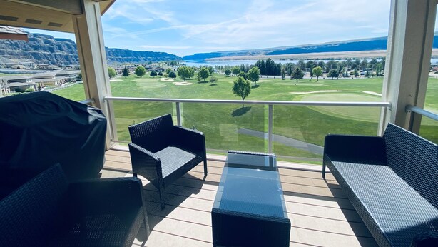 Een overdekt terras met rieten meubilair en uitzicht op een golfbaan.