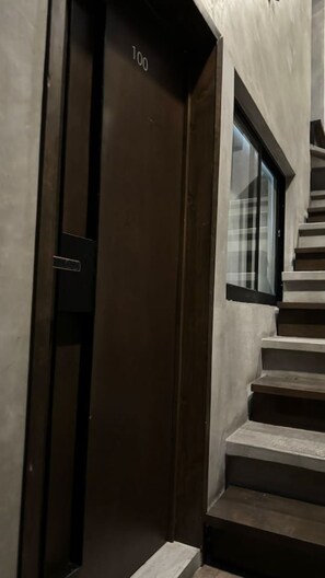 A staircase with a dark door marked '100' leading to a room with a large window.
