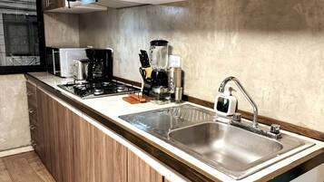 Una cocina moderna con estufa a gas, cafetera y pileta de acero inoxidable.