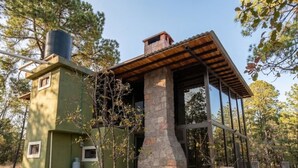 A rustic cabin with a stone chimney, wooden beams, and a metal roof structure. - Cabin La Promesa | Canyon Views (Durango)