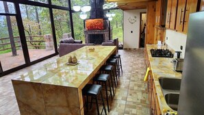 A spacious kitchen with a large island, a stone fireplace, and a view of the outdoors. - Cabin La Promesa | Canyon Views (Durango)