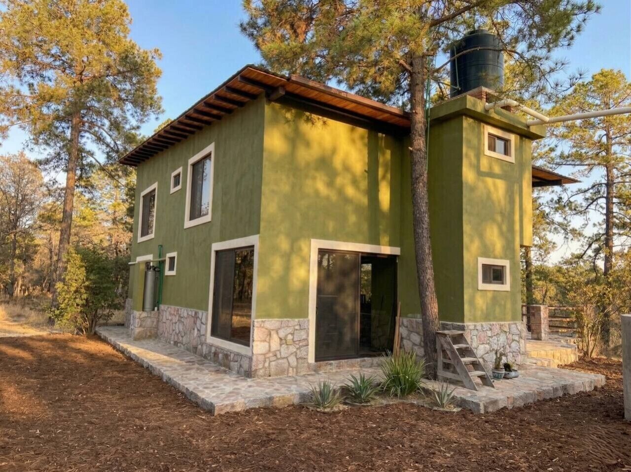 A two-story building with a stone foundation, a green exterior, and a wooden roof.