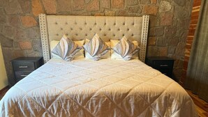A bed with a quilted headboard, flanked by two nightstands, in a room with stone wall decor. - Cabin La Promesa | Canyon Views (Durango)