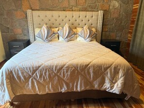 A bed with a quilted headboard, flanked by two nightstands, in a room with stone wall decor.