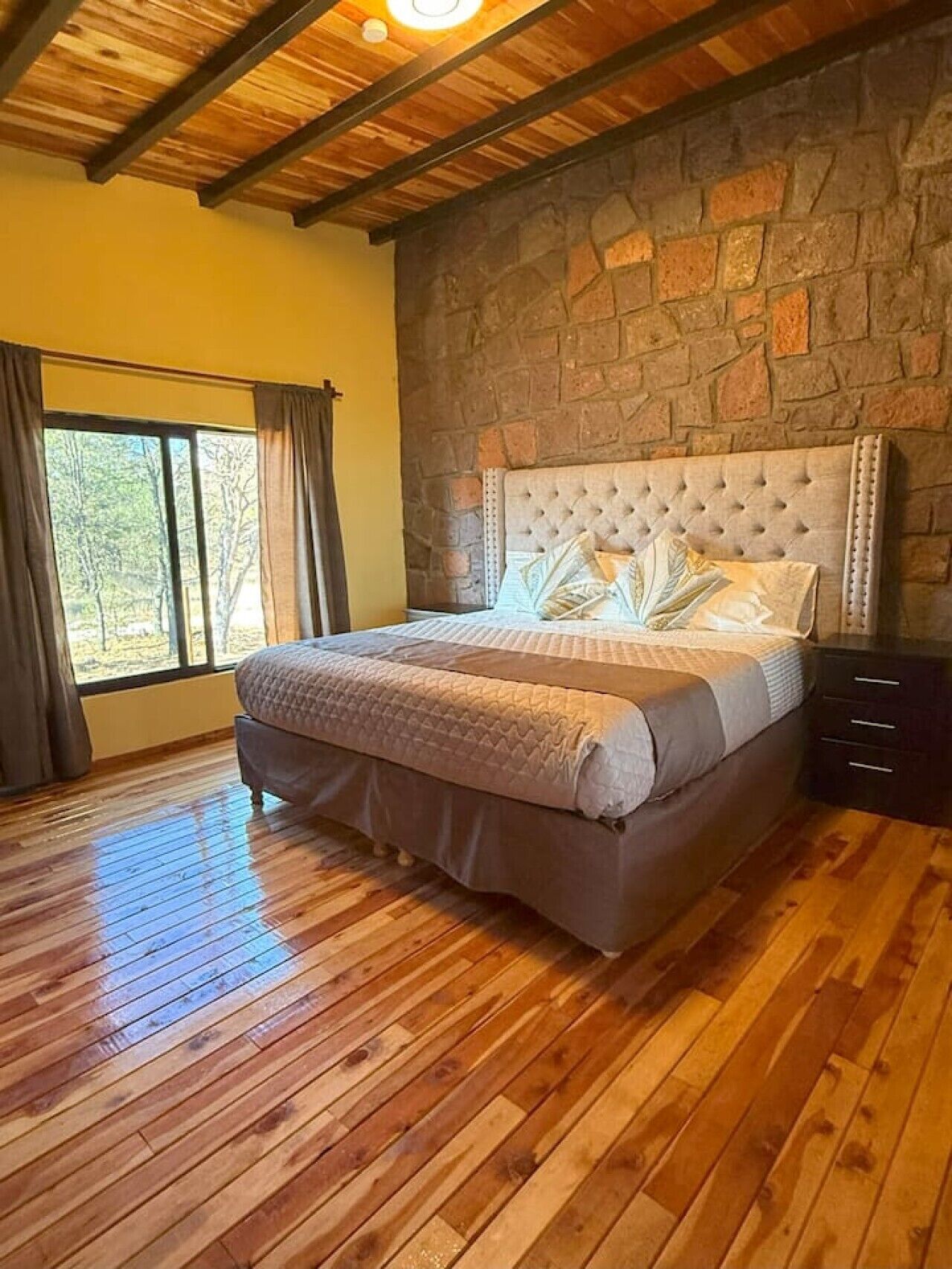 Quarto com parede de pedra, teto de madeira e cama com cabeceira.