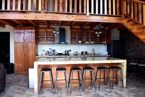 A wooden kitchen with a large island, bar stools, and a stone wall.