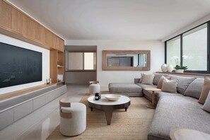 Ein modernes Wohnzimmer mit einem großen Flachbildfernseher, einer Eckcouch, einem Couchtisch und einem großen Fenster, das natürliches Licht hereinlässt.