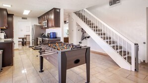 A modern kitchen with a foosball table, a dining area, and a staircase leading to another level. - The Pool House New 2-Story Home Near Strip (Las Vegas)