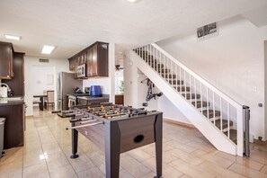 A modern kitchen with a foosball table, a dining area, and a staircase leading to another level. - The Pool House New 2-Story Home Near Strip (Las Vegas)