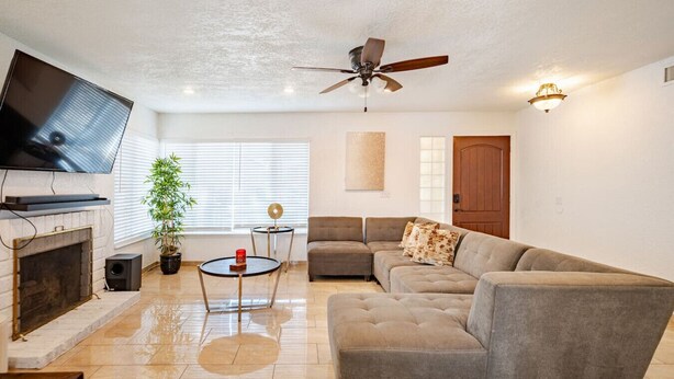 A living room with a sofa, TV, fireplace, and ceiling fan. - The Pool House New 2-Story Home Near Strip (Las Vegas)