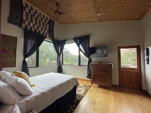 Ein Schlafzimmer mit Bett, Kommode, Fernseher und einem fenster mit Vorhängen.